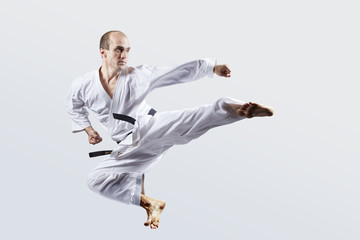 Adult athlete trains a kick in a jump against a light background