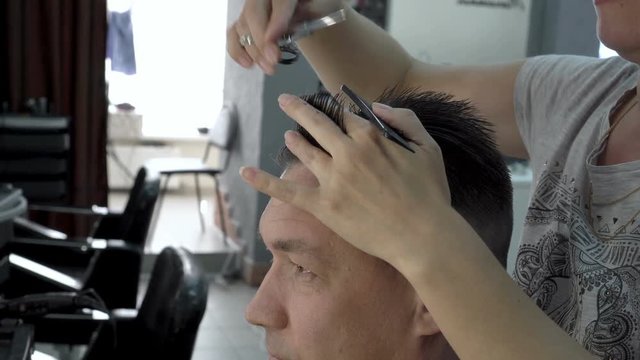 Woman hairdresser cuts hair of a man in a beauty salon. She combs her hair with a comb and cuts it with scissors. Hair care. Side view. 4K, 25 fps.