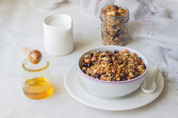 Breakfast: fresh oat granola in bowl with nuts, dried fruits, seeds and honey with milk in a on light background.