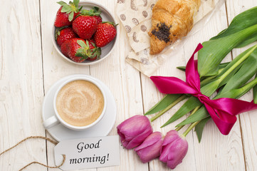 Cup of coffee, tulips, croissant, strawberries and Good morning massage on wooden background