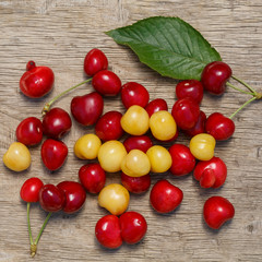 A lot of berries of red and white cherries are scattered over a old wooden surface of the table