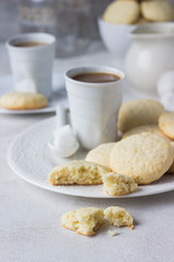 Plate with homemade coconut cookies and a cup of coffee with milk on a light background.