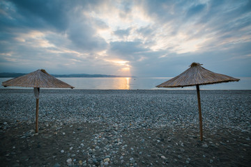 Umbrellas with a cane roof stand on the beach by the sea at dawn