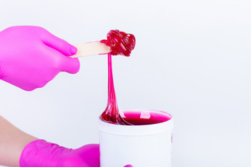 hands in crimson gloves holding a jar with sticky paste for sugaring isolated on white background.