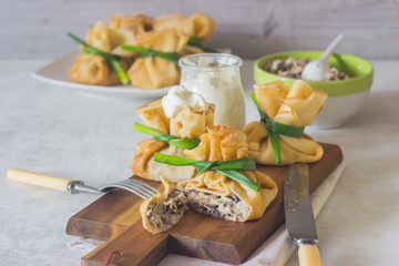 Crepes (pancakes) stuffed with chicken and mushrooms on a wooden cutting board served with sour cream. Traditional food on a pancake week. Traditional dish of Slavic cuisine.