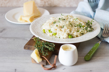 Homemade risotto with green peas, parmesan and thyme on a white plate and light background. 