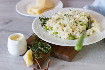 Homemade risotto with green peas, parmesan and thyme on a white plate and light background. 