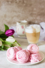 Obraz na płótnie Canvas Pink homemade zephyr or marshmallow with cup of cappuccino coffee and flowers on light gray background. Marshmallow, Meringue, Zephyr