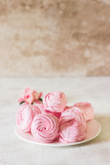 Beautiful delicious dessert. Pink zephyr on a white plate and pink flower. Berry zephyr on light gray background. 