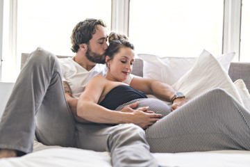 Man with pregnant woman in bed at home having great time
