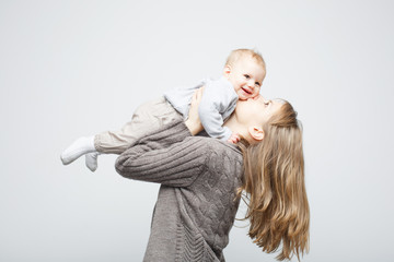 Happy beautiful young mother holding and kissing a baby girl standing over white background