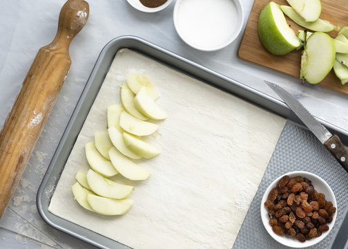 Preparation of apple strudel, apple slices layered on a sheet of pastry on a baking tray.