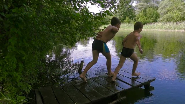 Two boys jump together to the river from pier