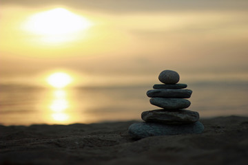 Obraz na płótnie Canvas Focused balanced cairns on beach in front of the sea by sunset/sunrise
