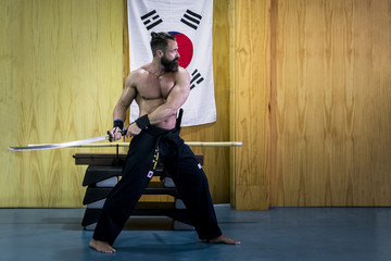 Hombre fuerte con grandes músculos entrenando artes marciales con katana. Defensa personal con...