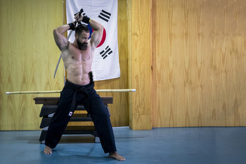 Hombre fuerte con grandes músculos entrenando artes marciales con katana. Defensa personal con...