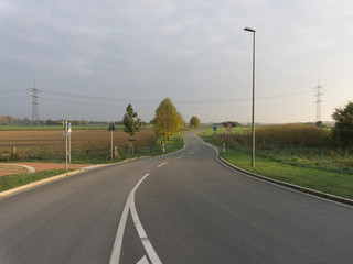 An empty road in a countryside at sunset among the fields