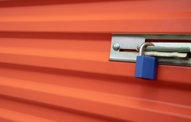Blue plastic lock on an orange self storage unit door.