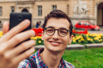 Handsome college man taking selfie in spring campus park. Happy guy student wearing glasses against university