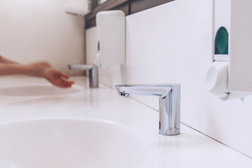 Sensor water tap in bathroom of cafe. Woman washing hands. Modern WC