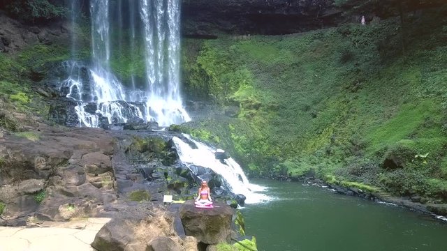 flycam rises above landscape with waterfall and girl on rock