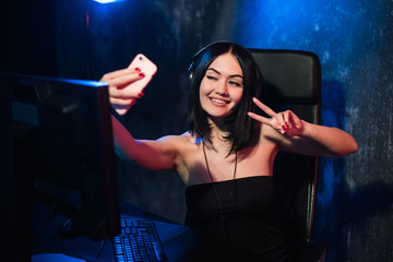 Cheerful gamer streamer girl wearing headset and sitting near her pc computer taking selfie on the phone during online game © romankosolapov