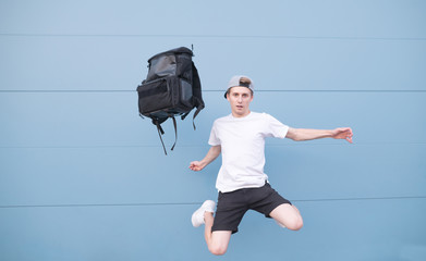 Man in a white T-shirt jumping with a backpack on a blue background. Backpack and a man flying...