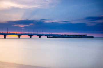 Obraz premium quiet beach with pier at sunset, long time exposure