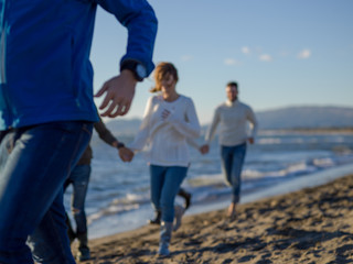 Group of friends running on beach during autumn day