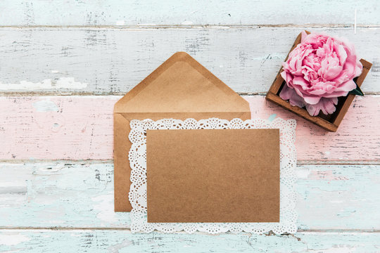 Flat lay empty card invitation with envelope. Festive background with sweet pink peonies flowers .Top view with place for text.