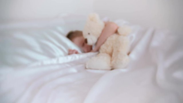 Seven-year-old boy wakes up hugging toy bear. Blur.