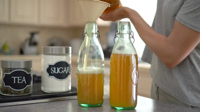 Female pours kombucha tea into two glass bottles 