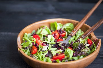 Fresh mixed pomegranate salad and cherry tomatoes on a wooden plate, pouring olive oil