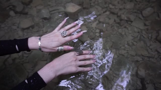 Female hands with long finger nails moving in the backgroung of water