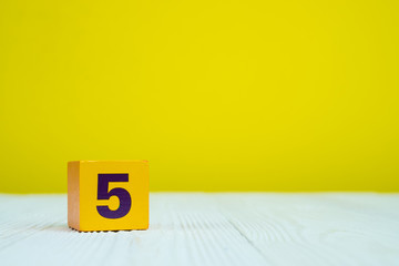 Square block puzzle number 5 on table with yellow background
