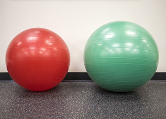 Small red exercise ball beside a medium size swiss ball in the gym