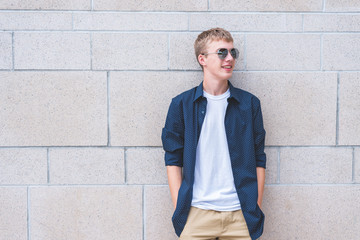 Happy teen wearing sunglasses leaning with his back against a brick wall.