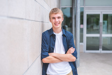 Happy teen with arms crossed leaning against brick wall of public building.