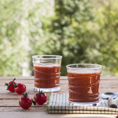 Delicious homemade tomato juice with salt on a striped napkin on a wooden table on a green foliage background. Selective focus. Close up.