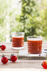 Delicious homemade tomato juice with salt on a striped napkin on a wooden table on a green foliage background. Selective focus. Close up.