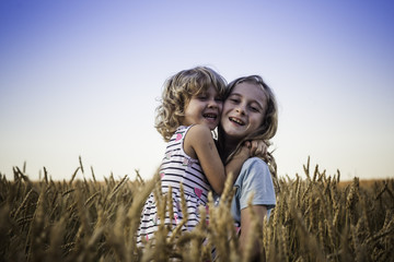 Two girls smiling and hugging in the wheat
