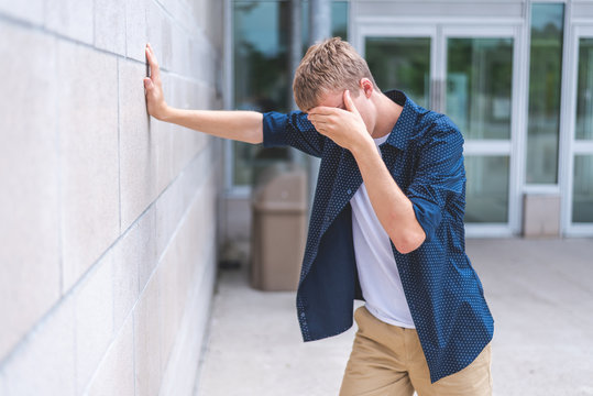 Upset Teen Leaning Against A Brick Wall Outside Of A Public Building.