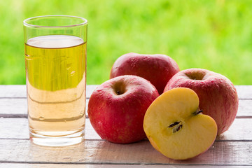 Glass of apple juice and red apples on wooden table with natural green background