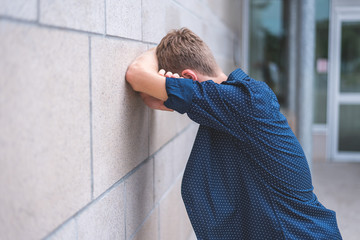 Teen crying into folded arms against a brick wall.