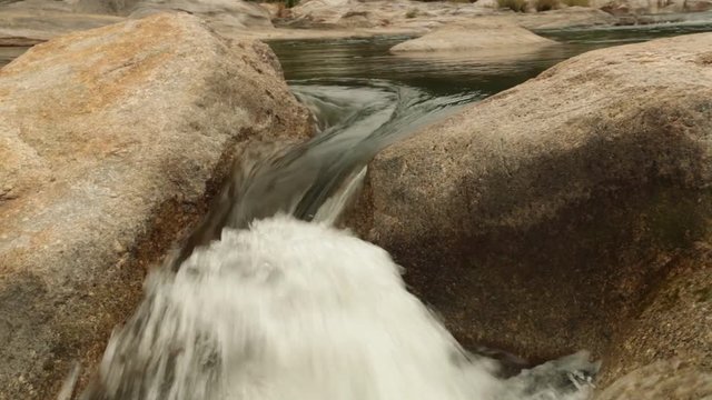 High definition panning action rugged mountain river waterfalls panoramic scene, with rushing white water cascading around large pebbles, boulders. Stock footage HD video clip.