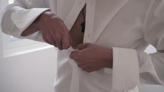 fit muscular male getting dressed for wedding or special event in white suit and tuxedo
