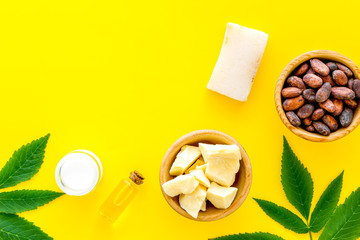 Cosmetics with cocoa butter for skin care. Cocoa beans and cocoa butter in bowl, soap, cream, oil or lotion in small bottles on yellow background top view copy space