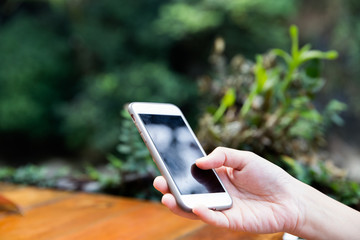 Female hand holding a mobile phone device on a wood table. Copy space for text.