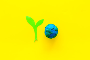 Planet, ecology. plastiline symbol of planet Earth globe and plant coutout on yellow background top view copy space