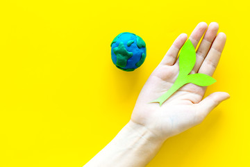 Planet, ecology. plastiline symbol of planet Earth globe and plant coutout on yellow background top view copy space